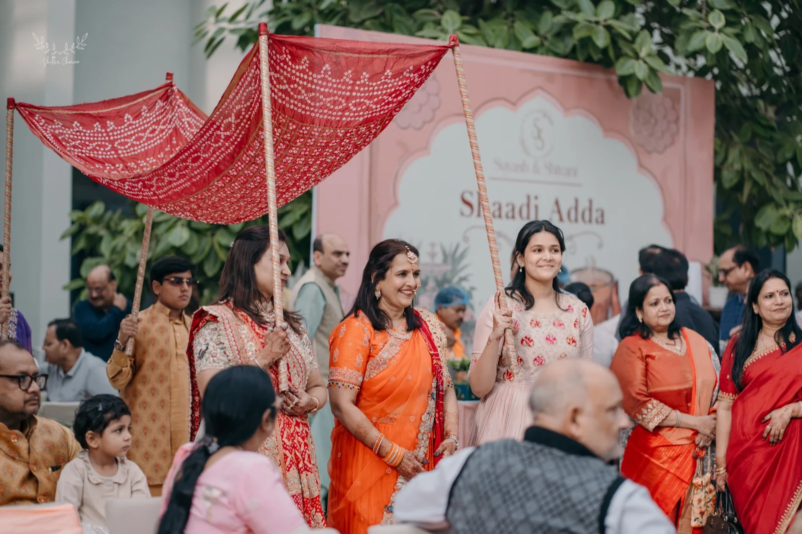 Smiling family members hold red bandhani canopy during bride entry