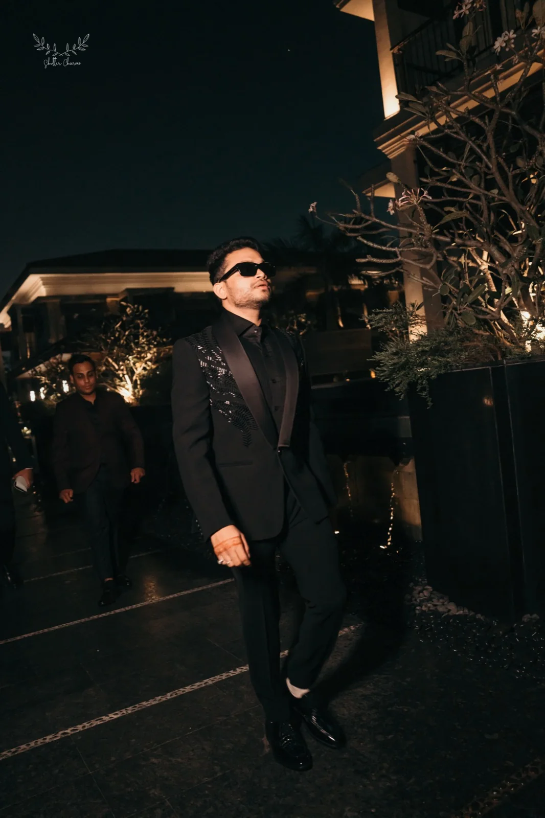 Groom in black tuxedo and sunglasses arriving at night reception