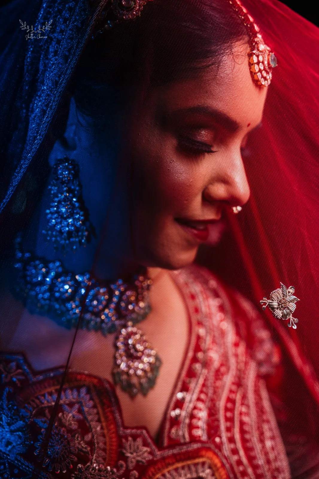 Bride smiling softly beneath sheer red veil with sparkling jewellery