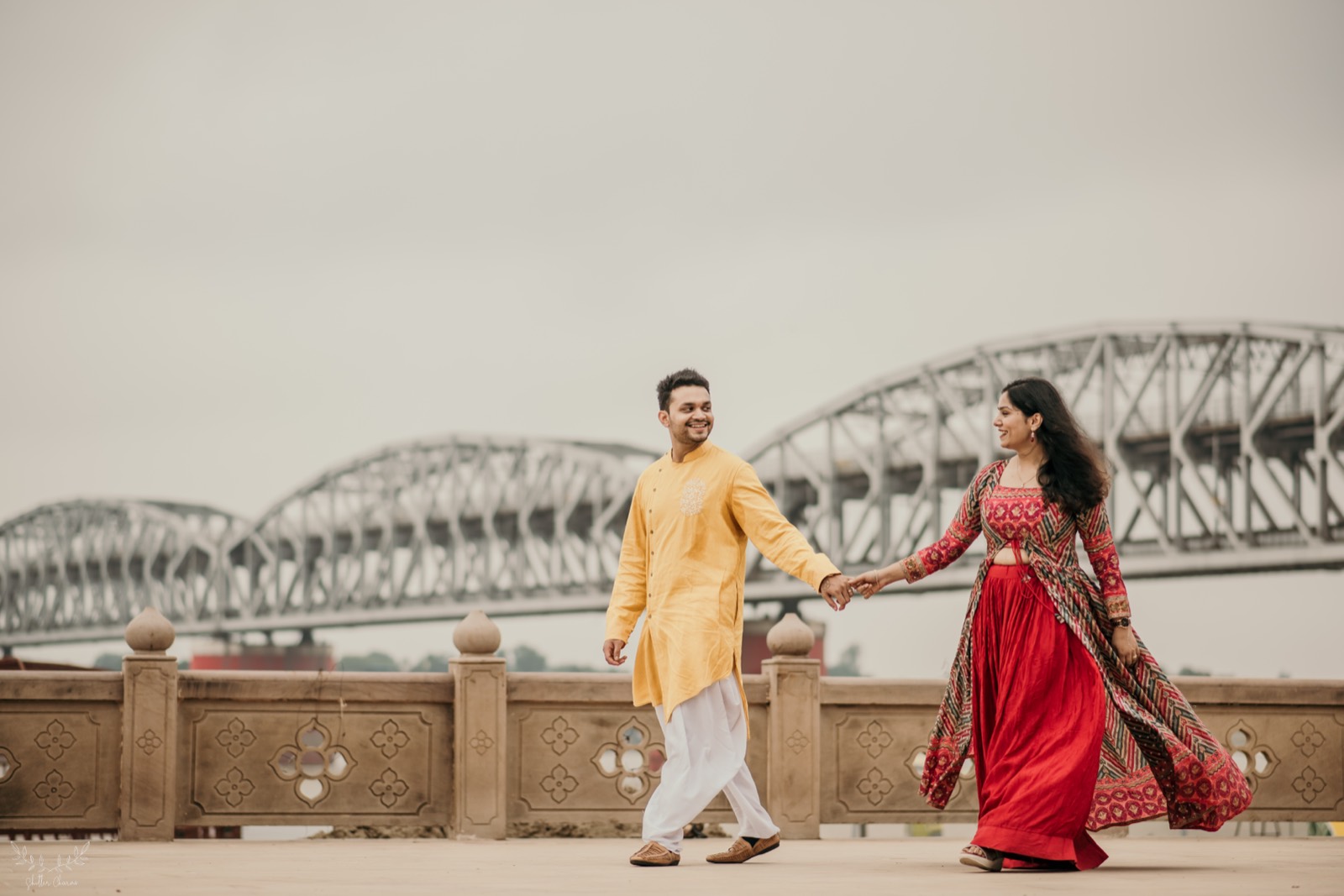 Couple walking hand in hand by riverside bridge during pre-wedding shoot