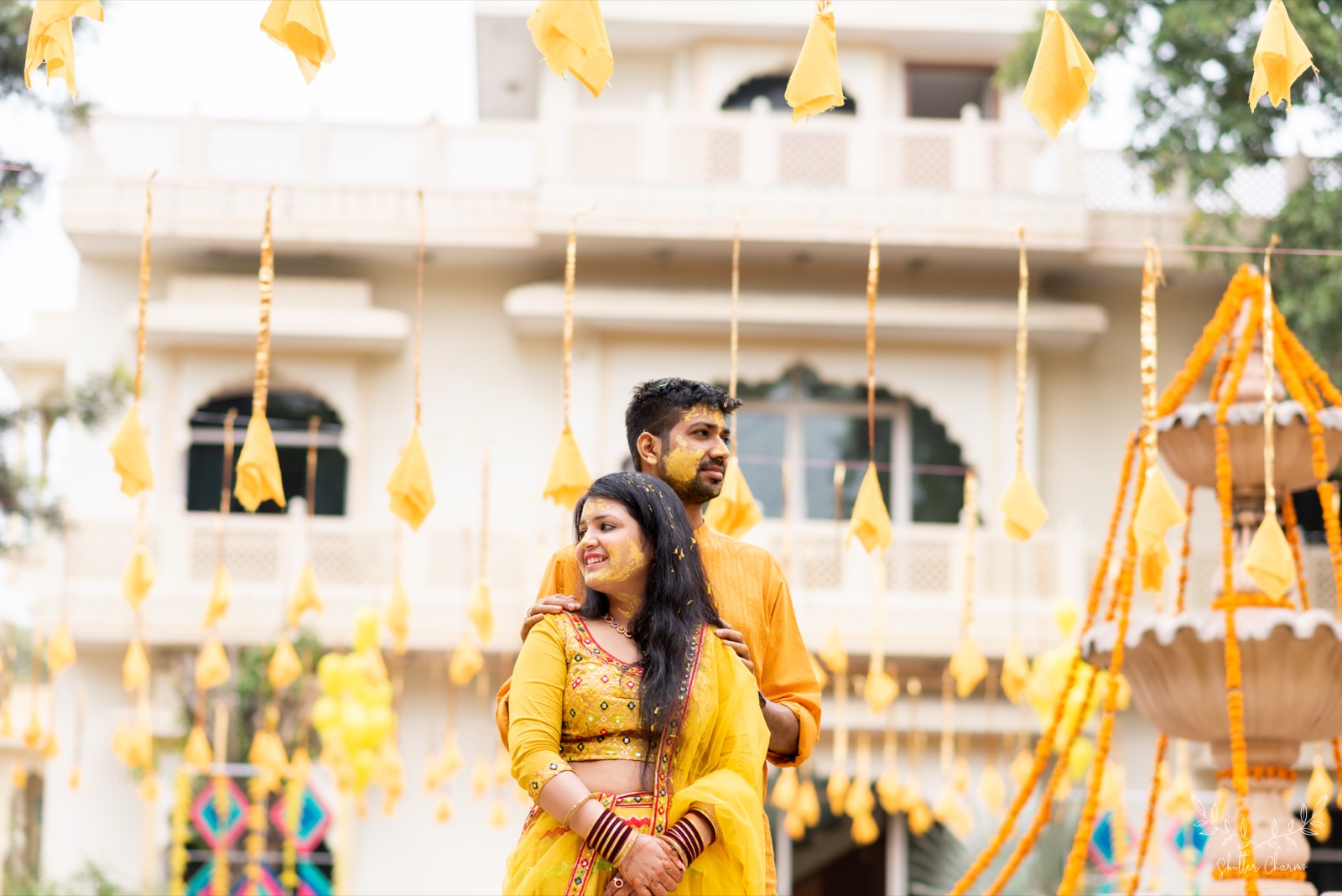 Haldi-smeared couple in yellow outfits posing amid marigold decor