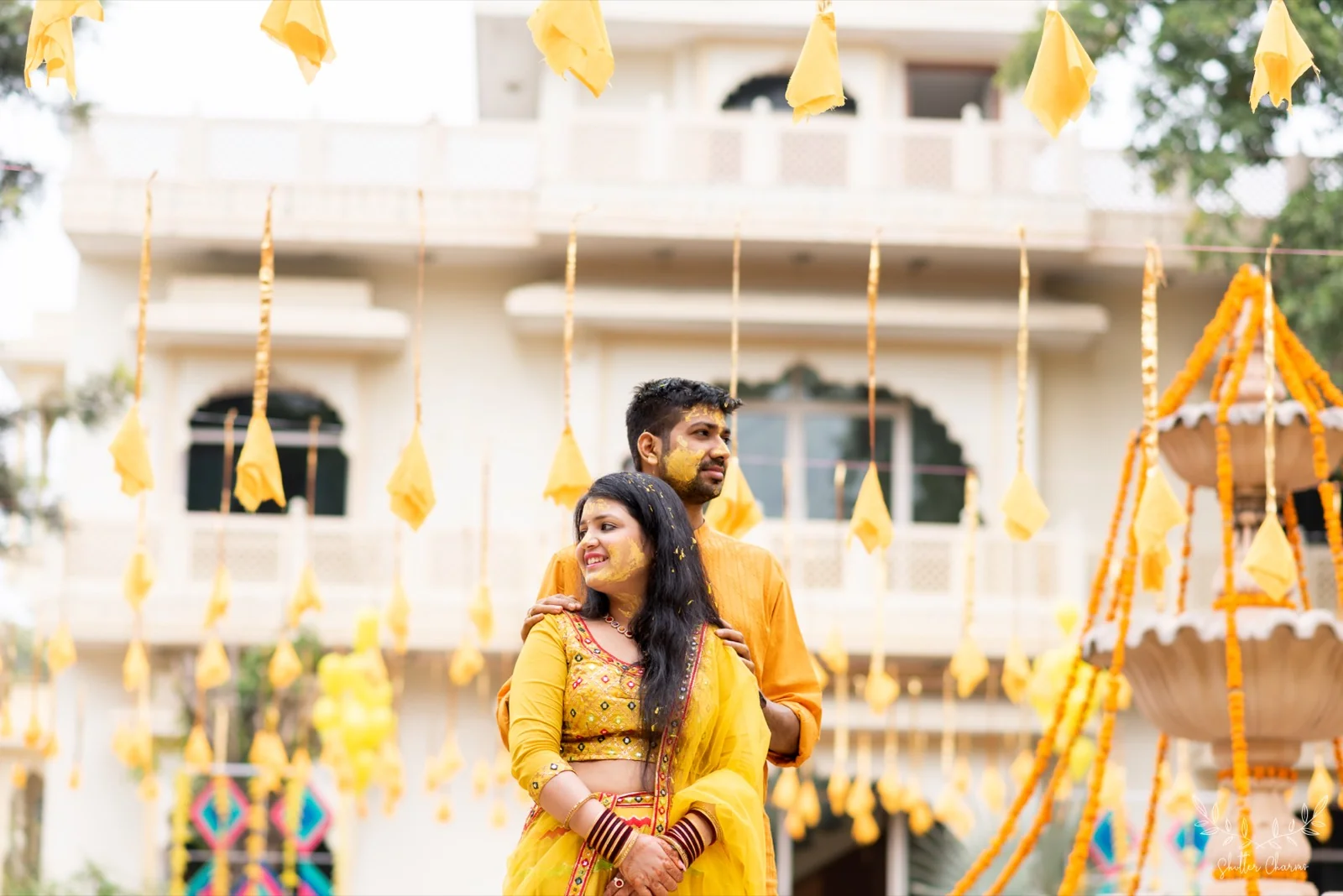 Haldi-smeared couple in yellow outfits posing amid marigold decor