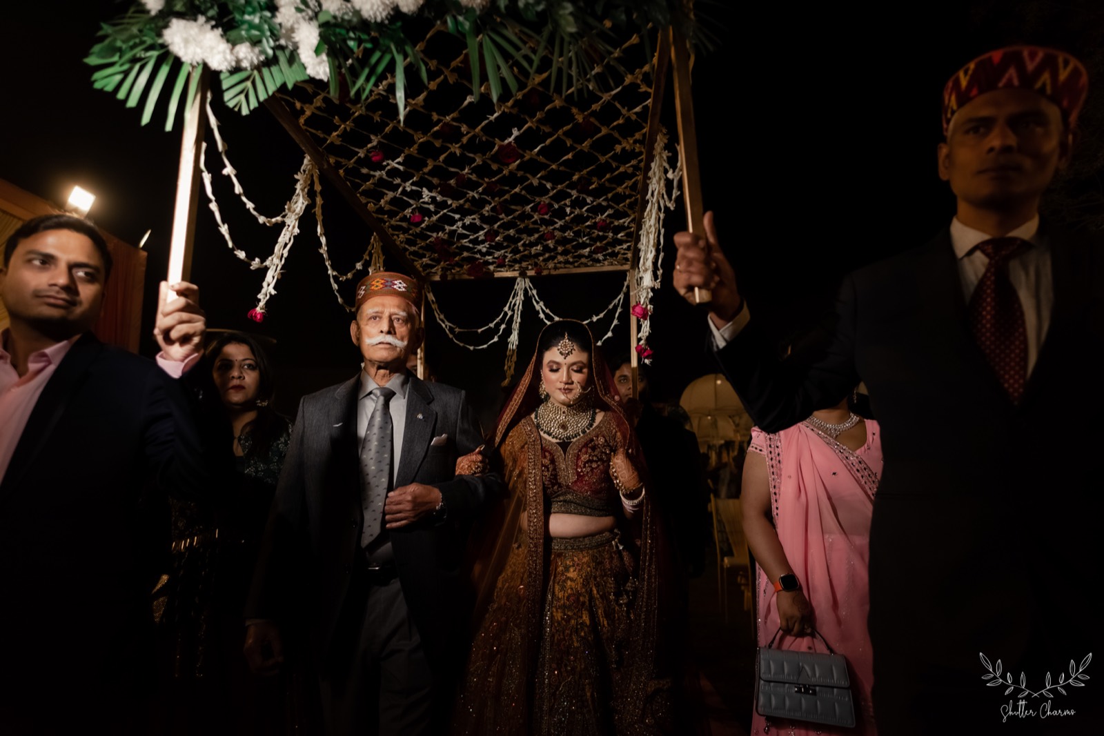Bride enters under a floral canopy escorted by family elders