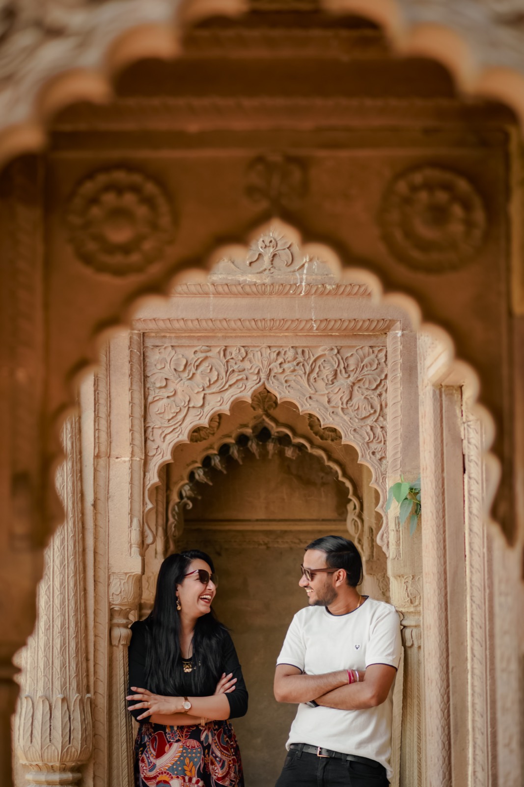 Couple laughing together under carved sandstone arches during pre-wedding shoot